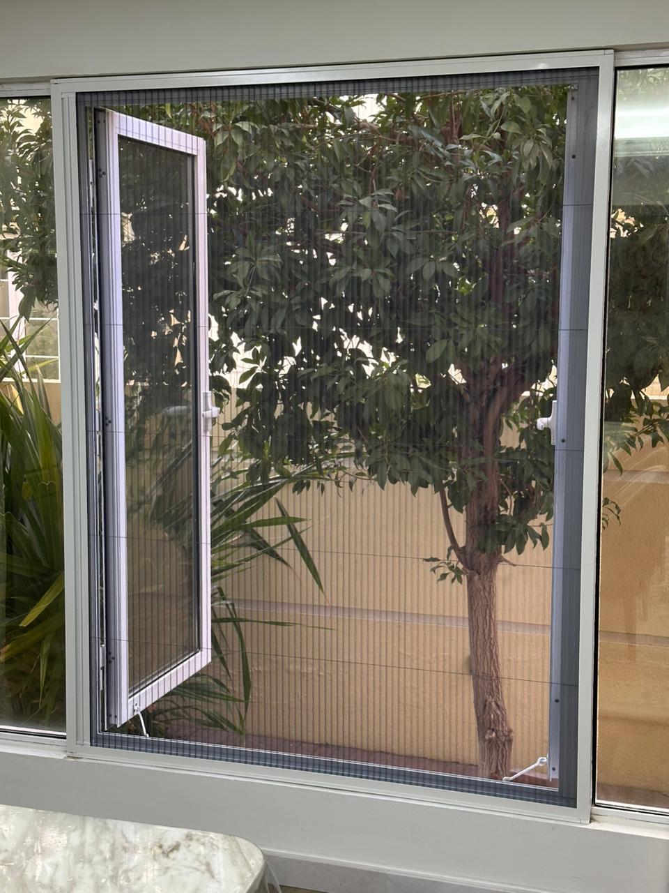 Pleated fly screen on an open casement window in a Dubai home showing garden view